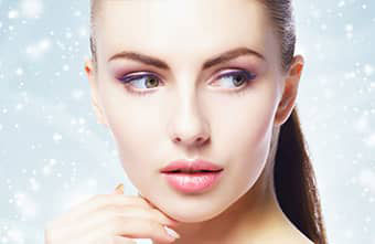 The image depicts a person with makeup and a neutral expression, set against a blurred background.
