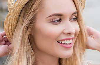 A woman with blonde hair wearing a straw hat and smiling at the camera.