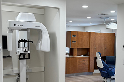The image shows a modern dental office interior with various pieces of equipment and furniture, including a dental chair, a dental machine, a large mirror, cabinets, and a patient waiting area.