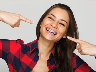 A smiling woman with a playful gesture pointing at her teeth, set against a white background.